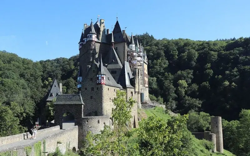 Eltz Castle in Germany rises from a forested valley with tall towers and stone walls.