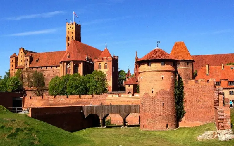 Malbork Castle in Poland shows red brick walls and towers under a blue sky.