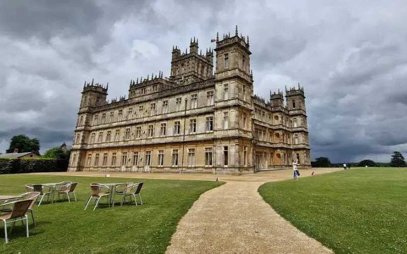 Highclere Castle surrounded by green lawns under a cloudy sky.