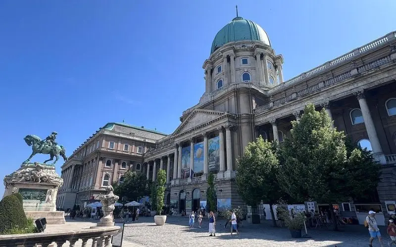Buda Castle in Hungary with a green dome and statue in the courtyard.