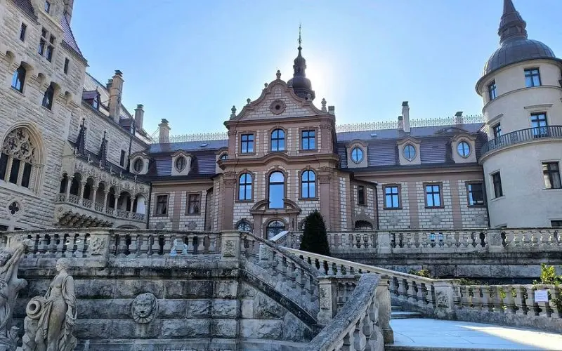 Moszna Castle in Poland with ornate architecture and stone steps.