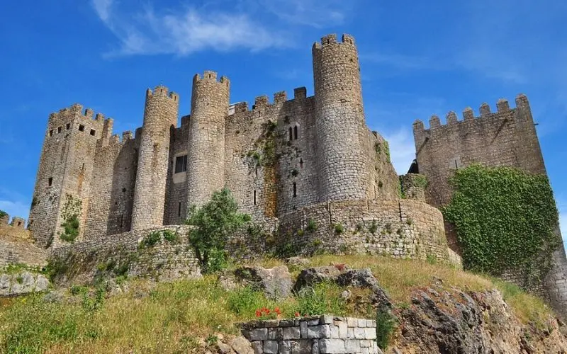 Óbidos Castle in Portugal with round stone towers and ivy-covered walls.
