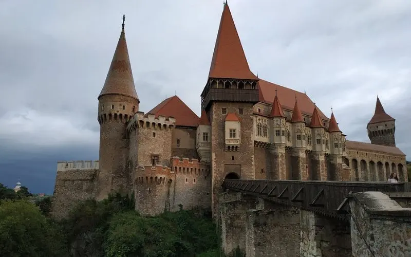 Corvin Castle in Romania with tall red-roofed towers and a bridge leading to the entrance.