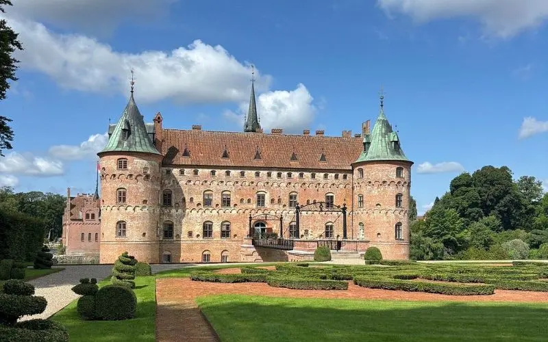 Egeskov Castle in Denmark with red brick walls, green towers, and a manicured garden.