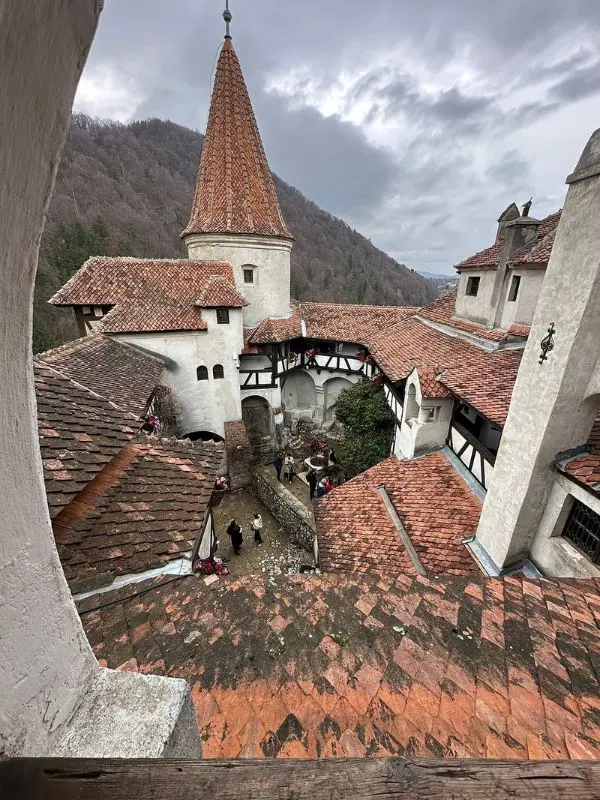 Bran Castle in Romania features red rooftops and a stone courtyard surrounded by hills.
