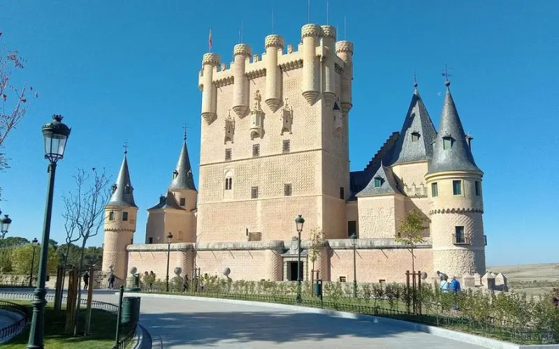 Alcázar of Segovia in Spain with tall spires and pale stone walls under a clear sky.