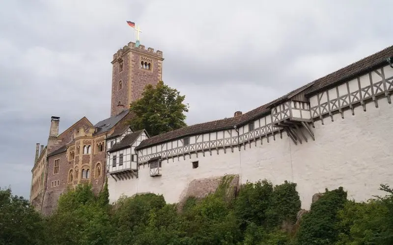 Wartburg Castle in Germany with a stone tower and half-timbered buildings along the wall.