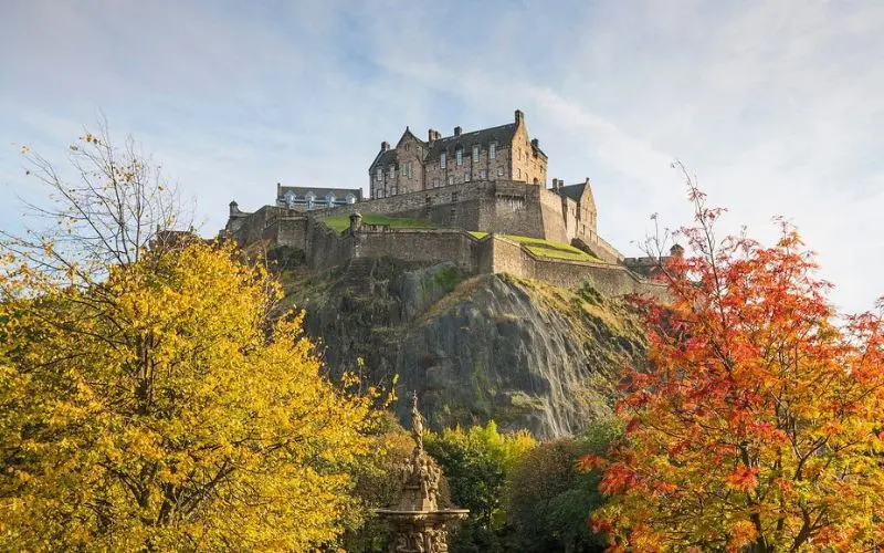 Edinburgh Castle in Scotland stands high on a rocky hill with autumn trees below.