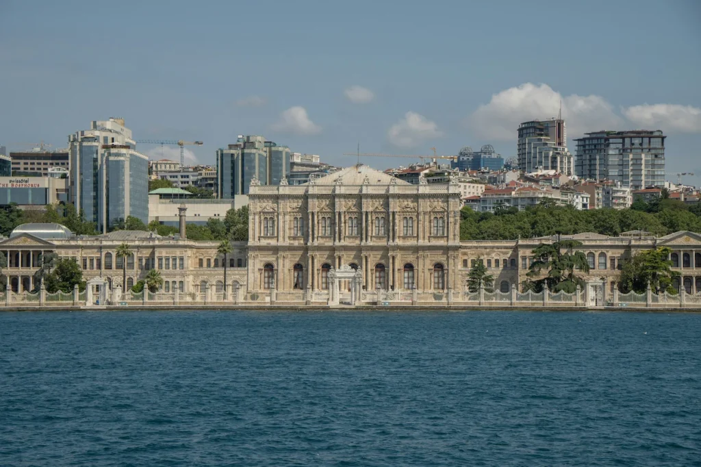 Waterfront view of Dolmabahçe Palace with Istanbul's hillside skyline under a blue sky