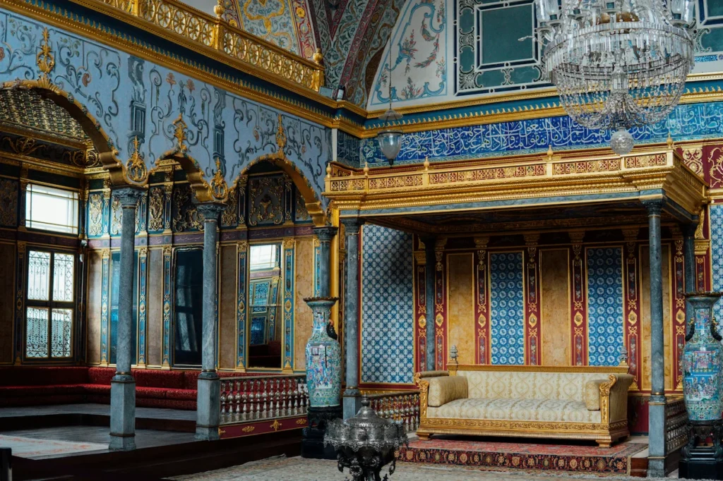 Ornate palace room with blue patterned tiles, golden arches, a crystal chandelier, and a gold sofa