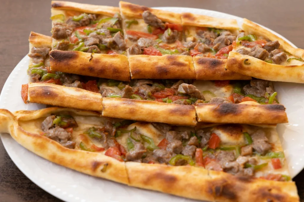 Sliced Turkish pide with diced meat, tomatoes, and green peppers on a white plate