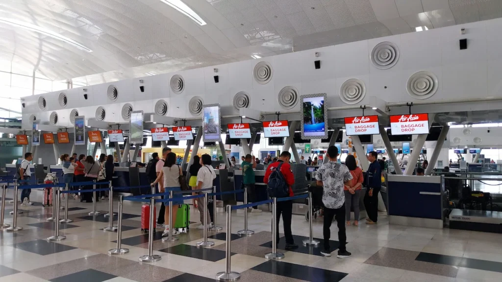 Passengers queuing with luggage at AirAsia baggage drop counters inside a modern airport terminal