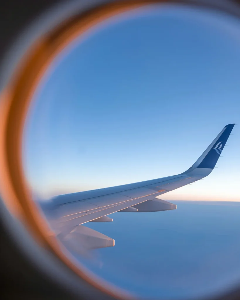 An Alaska Airlines wing with a blue wingtip logo framed through a round passenger window at sunset