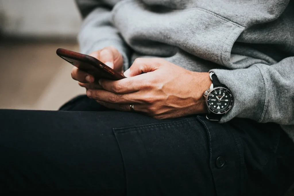 A close-up of a person wearing a black Seiko dive watch while typing on a smartphone