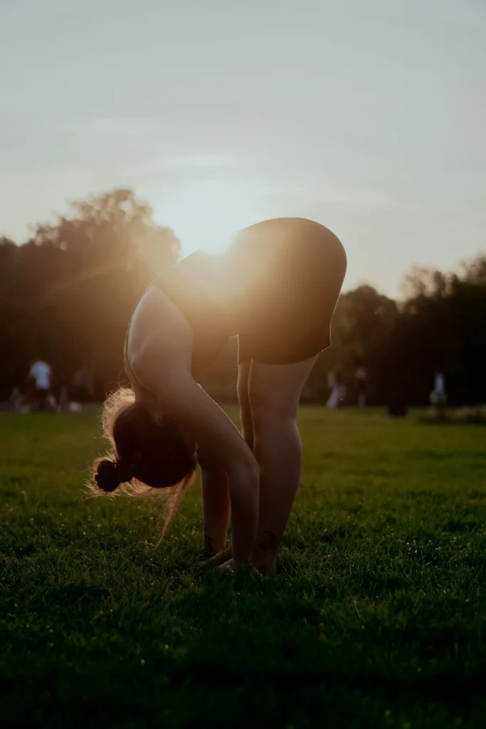 Woman doing a standing forward fold yoga stretch on green grass at sunset