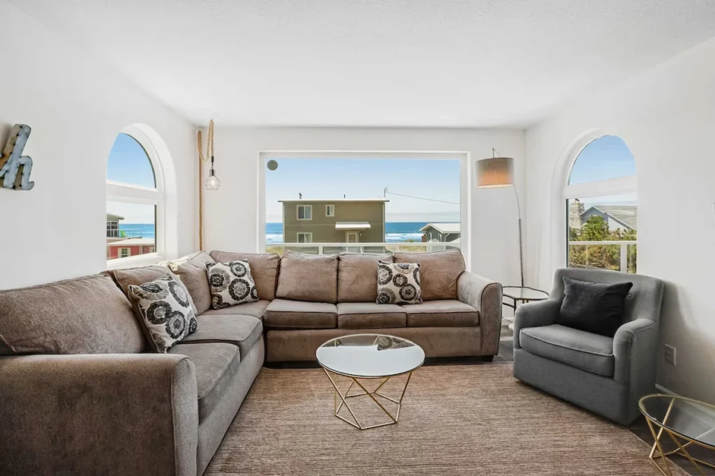 Bright beach house living room with a large sectional sofa, accent chair, and a picture window overlooking the ocean