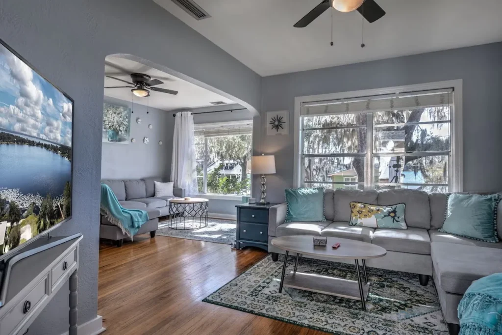 Two grey sectional sofas in a living room with hardwood floors and large windows