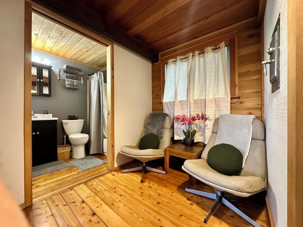 Two swivel chairs on hardwood floors next to an open doorway showing a cabin bathroom