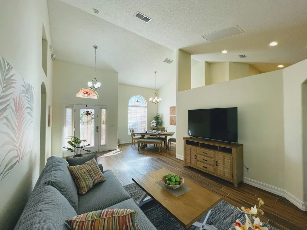 Open-concept living room with a grey sofa and television leading into a naturally lit dining area