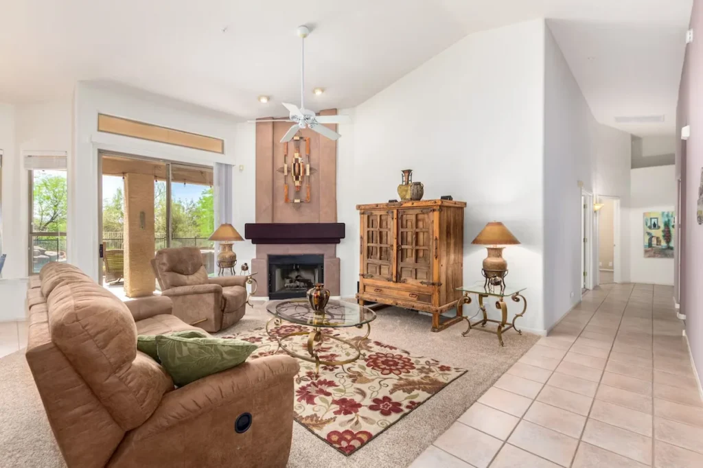 Spacious living room with tan reclining sofas, a tiled hallway, a wooden armoire, and a kiva-style fireplace