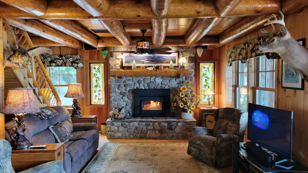 Rustic log cabin living room with an exposed log ceiling, a stone fireplace, and comfortable sofas