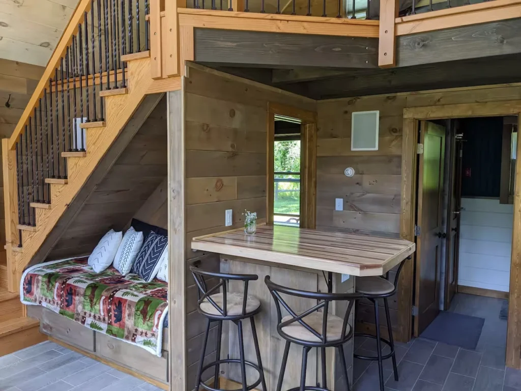 Cabin interior featuring a wooden kitchen breakfast bar with stools next to a cozy daybed nook tucked under the stairs
