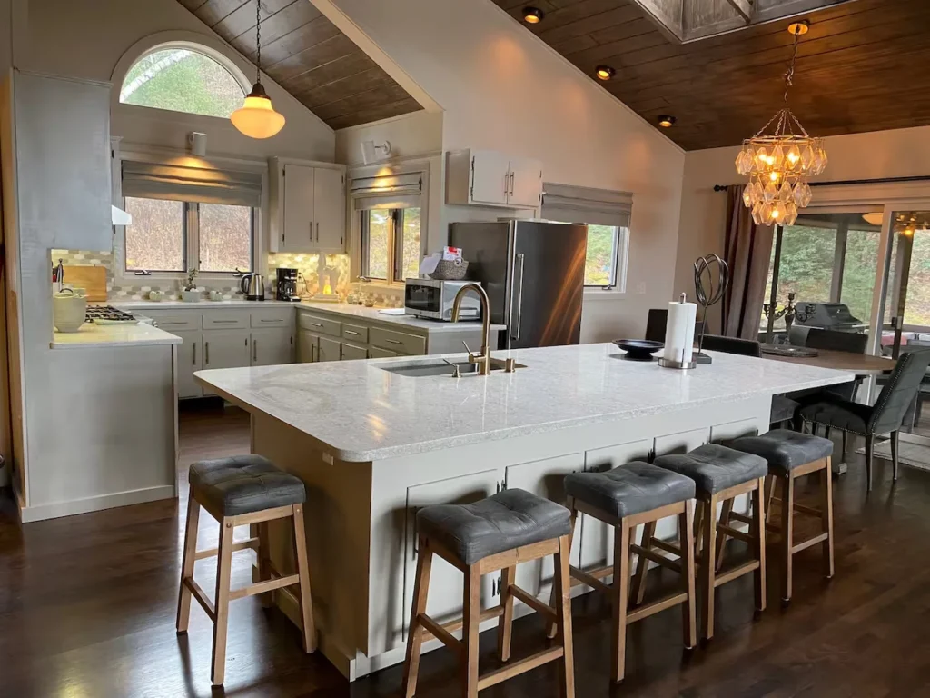 Large kitchen island with white quartz countertop and grey barstools under a vaulted wood ceiling
