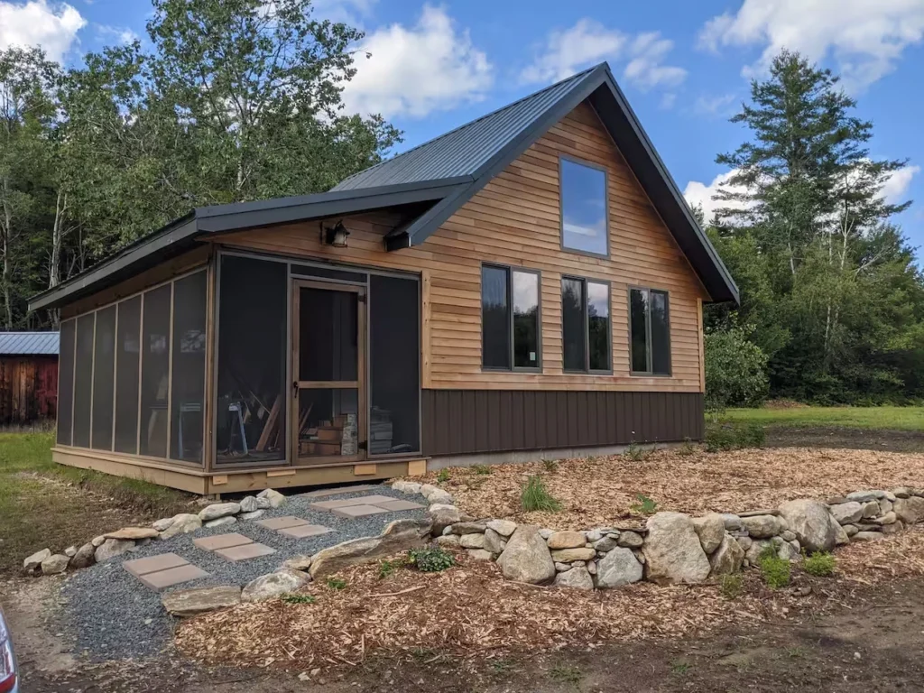 Modern A-frame wooden cabin featuring a screened porch addition and a stone retaining wall pathway