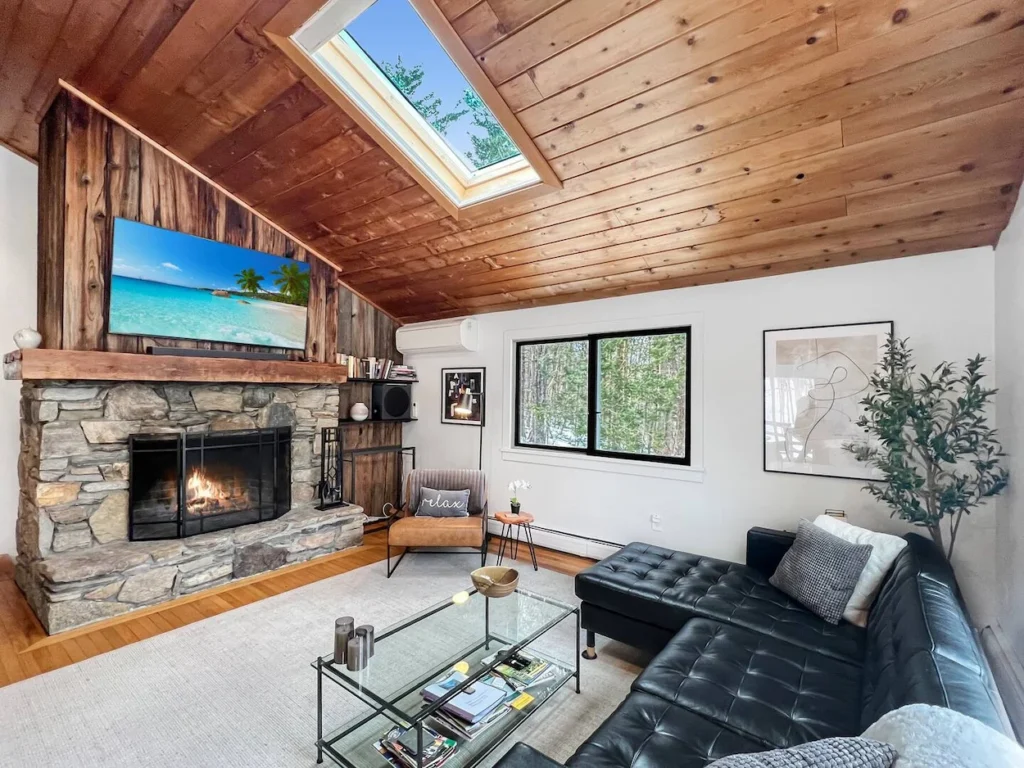 Chalet living room with a wood ceiling, stone fireplace, leather sectional, and skylight