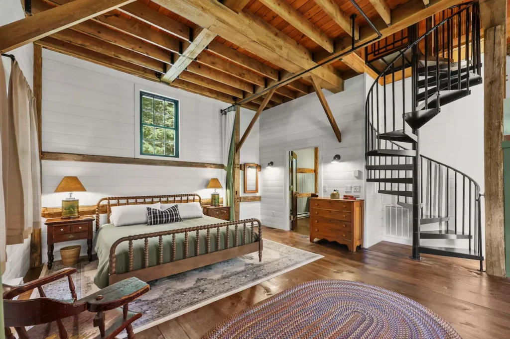 Rustic bedroom featuring a wooden spindle bed, exposed ceiling beams, and a black metal spiral staircase