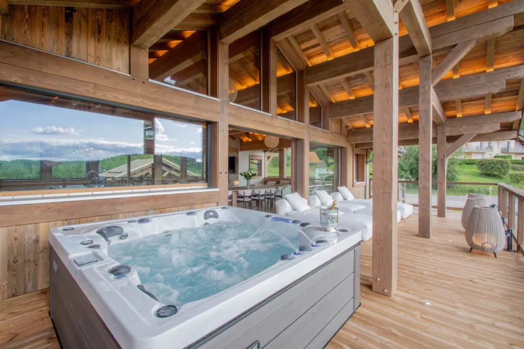 Chalet L'Ours Blanc covered wooden deck with a bubbling hot tub and outdoor lounge chairs