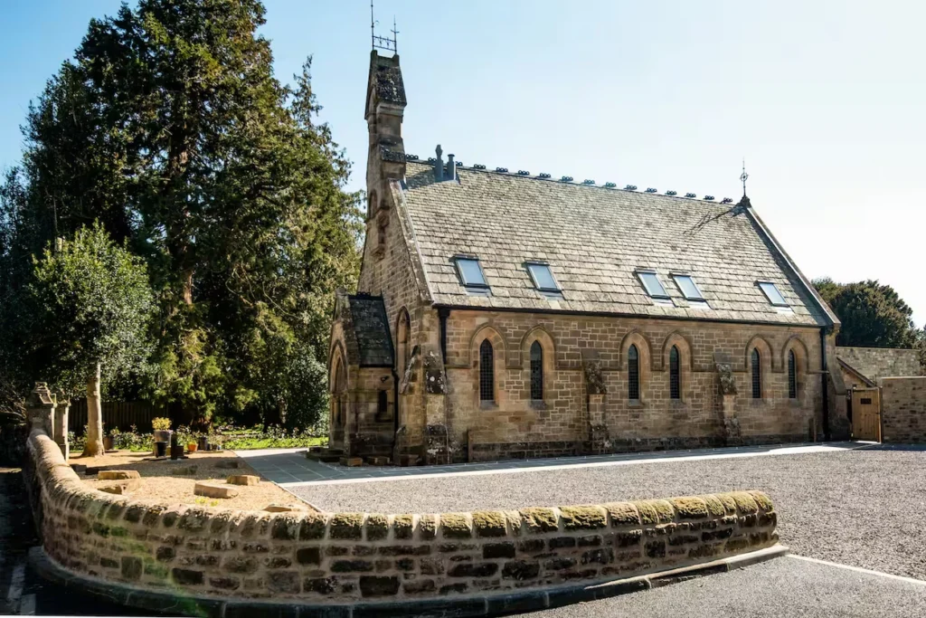 Stone exterior of Warksburn Old Church featuring arched windows, skylights, and a gravel driveway