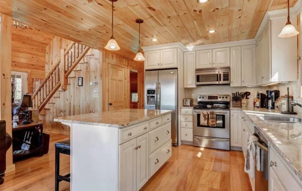 Cabin kitchen featuring white cabinets, a central island, granite countertops, and stainless steel appliances