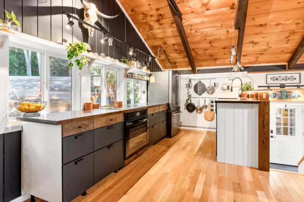 Cabin kitchen featuring black lower cabinets, wood ceilings, stainless refrigerator, and open hanging pot rack