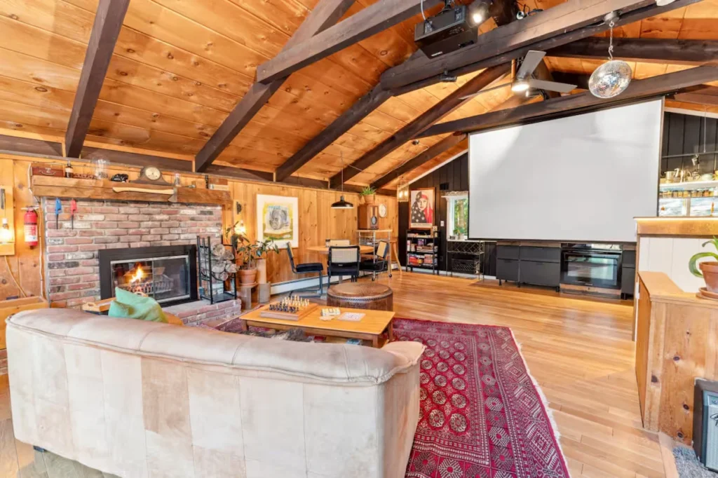 Cabin living room with wood walls, brick fireplace, tan sofa, red rug, and projector screen