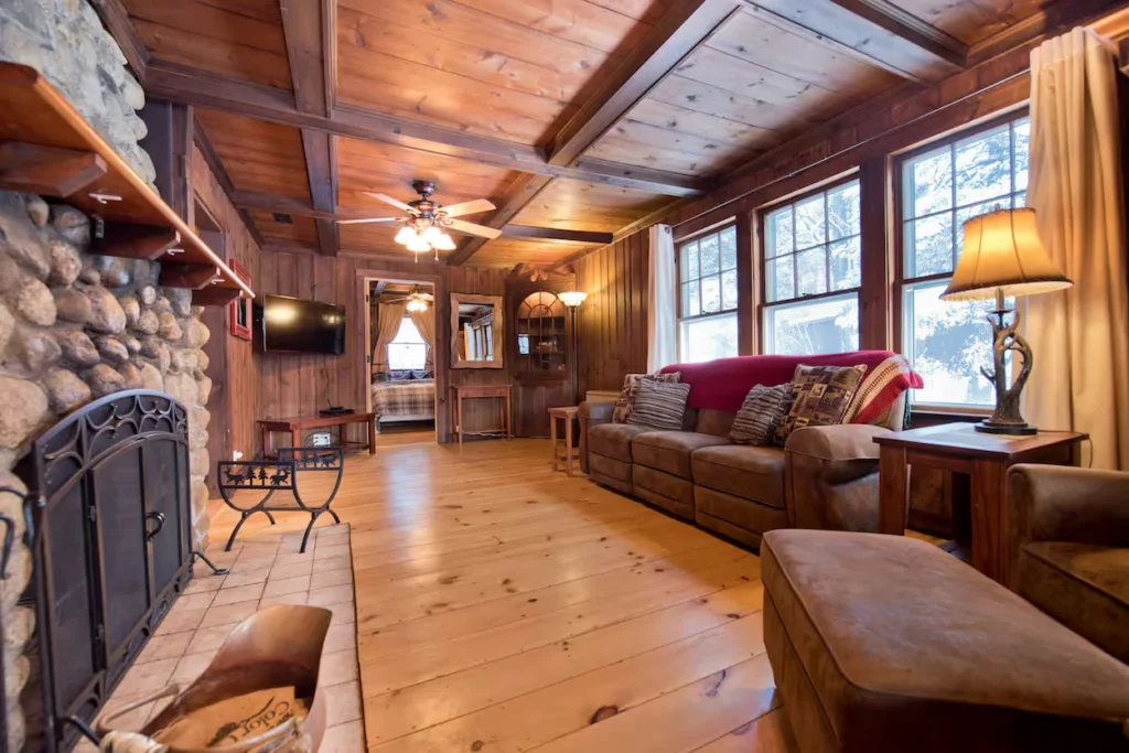 Rustic living room featuring a river stone fireplace, brown sofas, and a wood ceiling with a fan