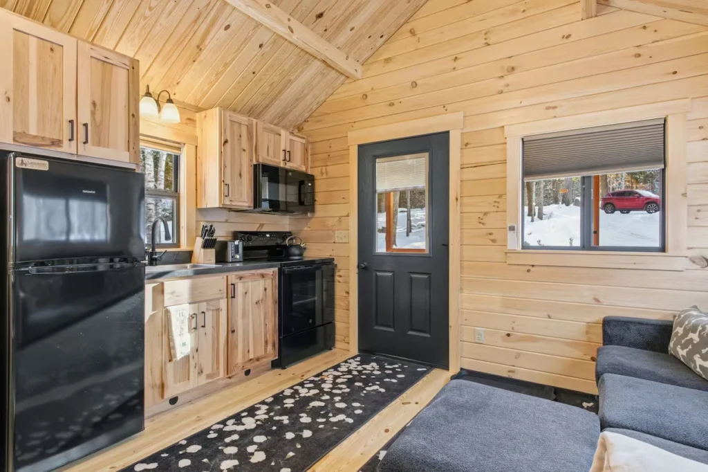 Small cabin interior with light wood walls, black kitchen appliances, and a grey sofa