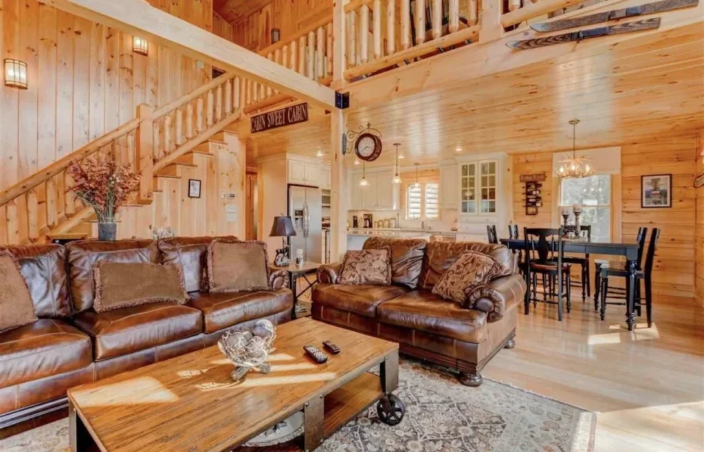 Cabin living room with brown leather couches, wood stairs, and a dining set