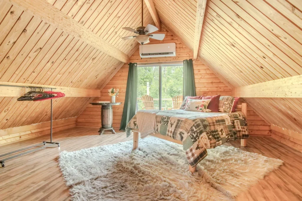 Cabin loft bedroom with wood paneled walls, a patterned quilt bed, and a shag rug