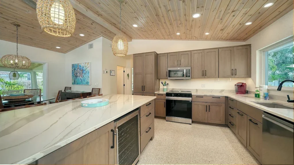 A modern cottage kitchen with a marble-topped island, wooden cabinets, and woven pendant lighting