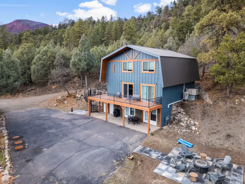 Blue two-story mountain home with a wooden deck and a stone patio fire pit area