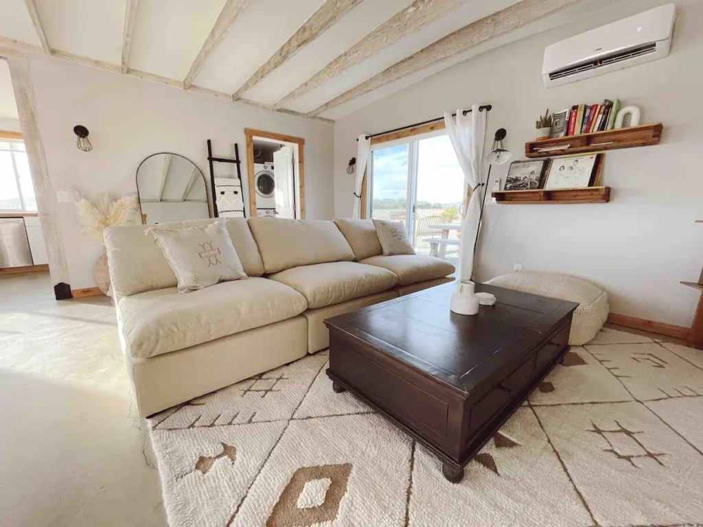 Bright living room with a large beige sectional sofa, dark wood coffee table, and exposed ceiling beams