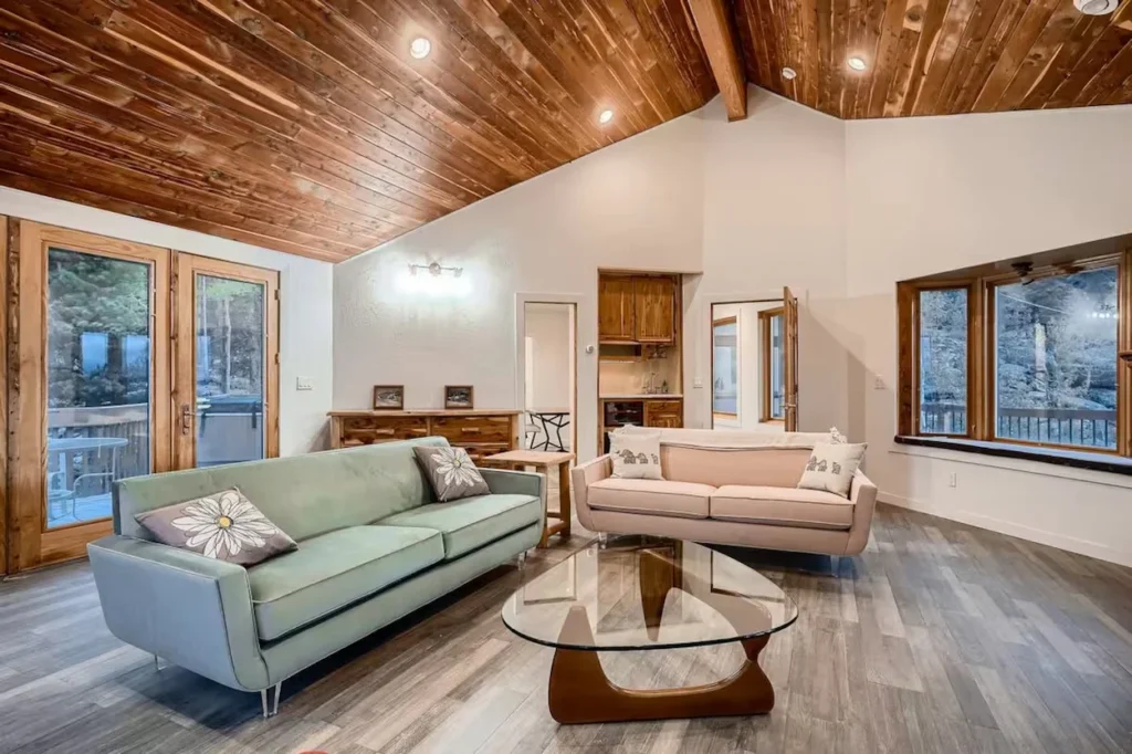 Sage green and pink sofas facing a glass coffee table in a vaulted cabin living room