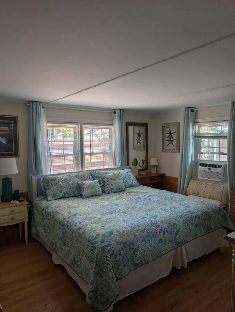 Bright cottage bedroom featuring a large king bed with a blue pattern quilt and matching curtains