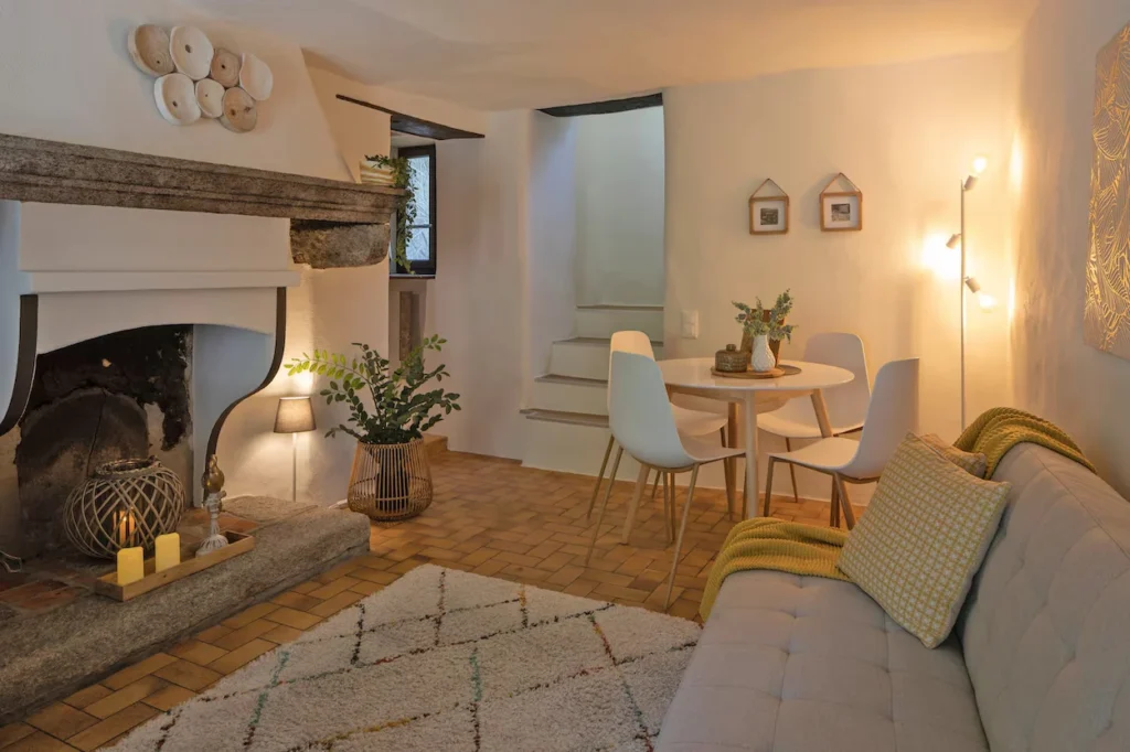 Cozy home interior featuring a historic stone fireplace, tile floor, and a small dining table with white chairs