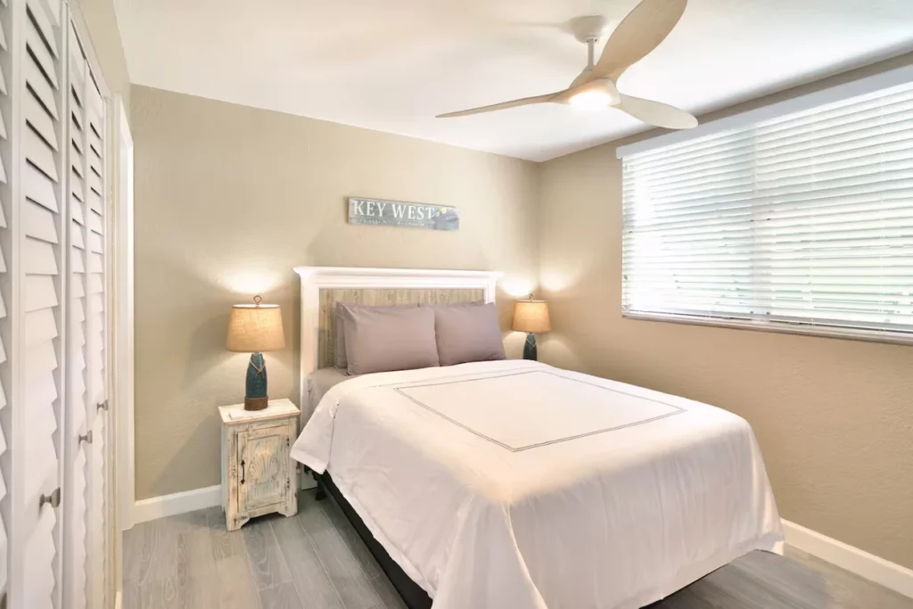 Cozy bedroom with a white headboard, bedside lamps, and a Key West sign on the wall
