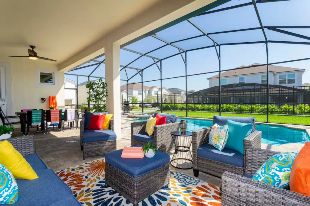A screened-in patio with grey wicker sofas, colorful pillows, an outdoor dining table, and a private pool