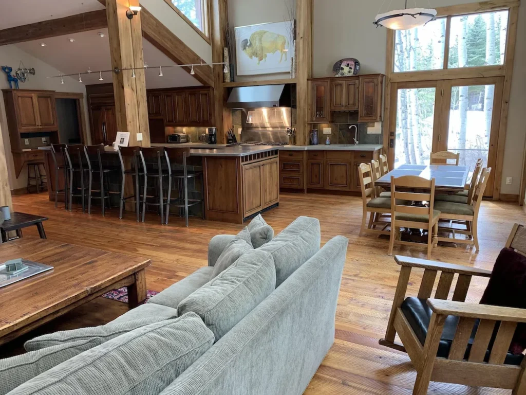 Spacious cabin interior with vaulted ceilings, large kitchen island, dining table, and green sectional sofa