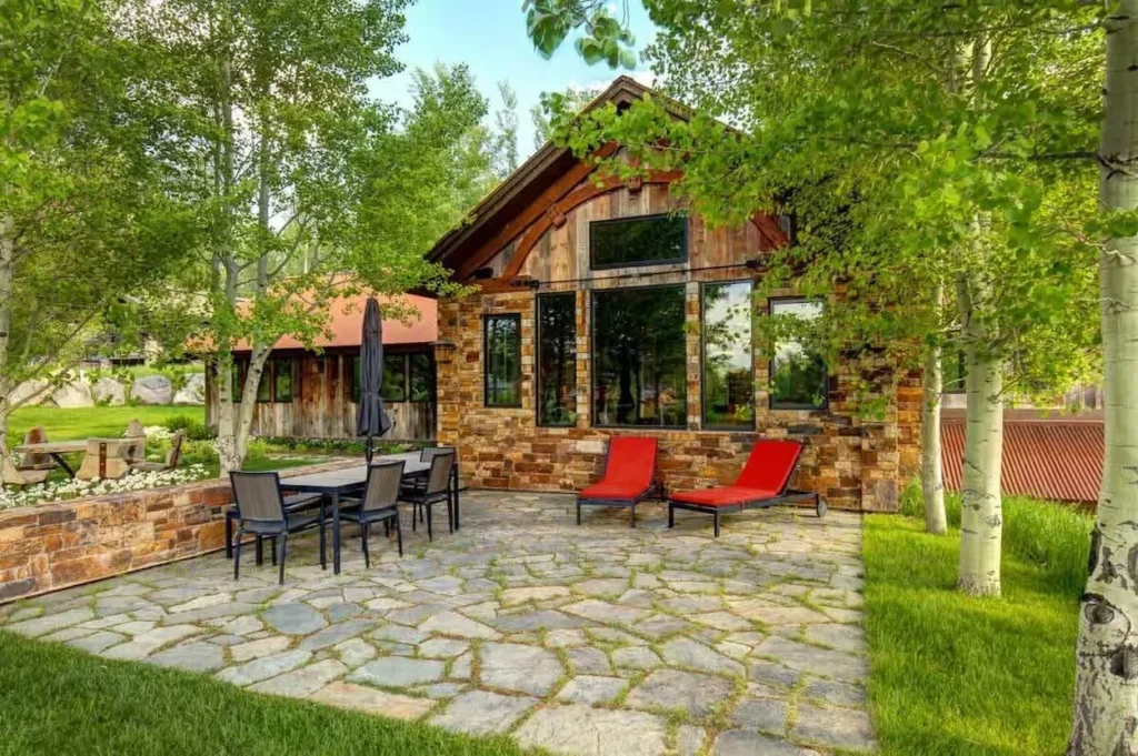 Stone patio with an outdoor dining table and red lounge chairs outside a rustic stone-and-timber mountain lodge