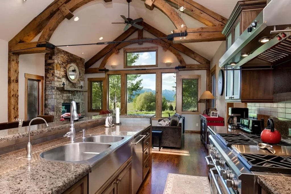Open-concept cabin kitchen with large island and stone fireplace under massive arched wooden beams